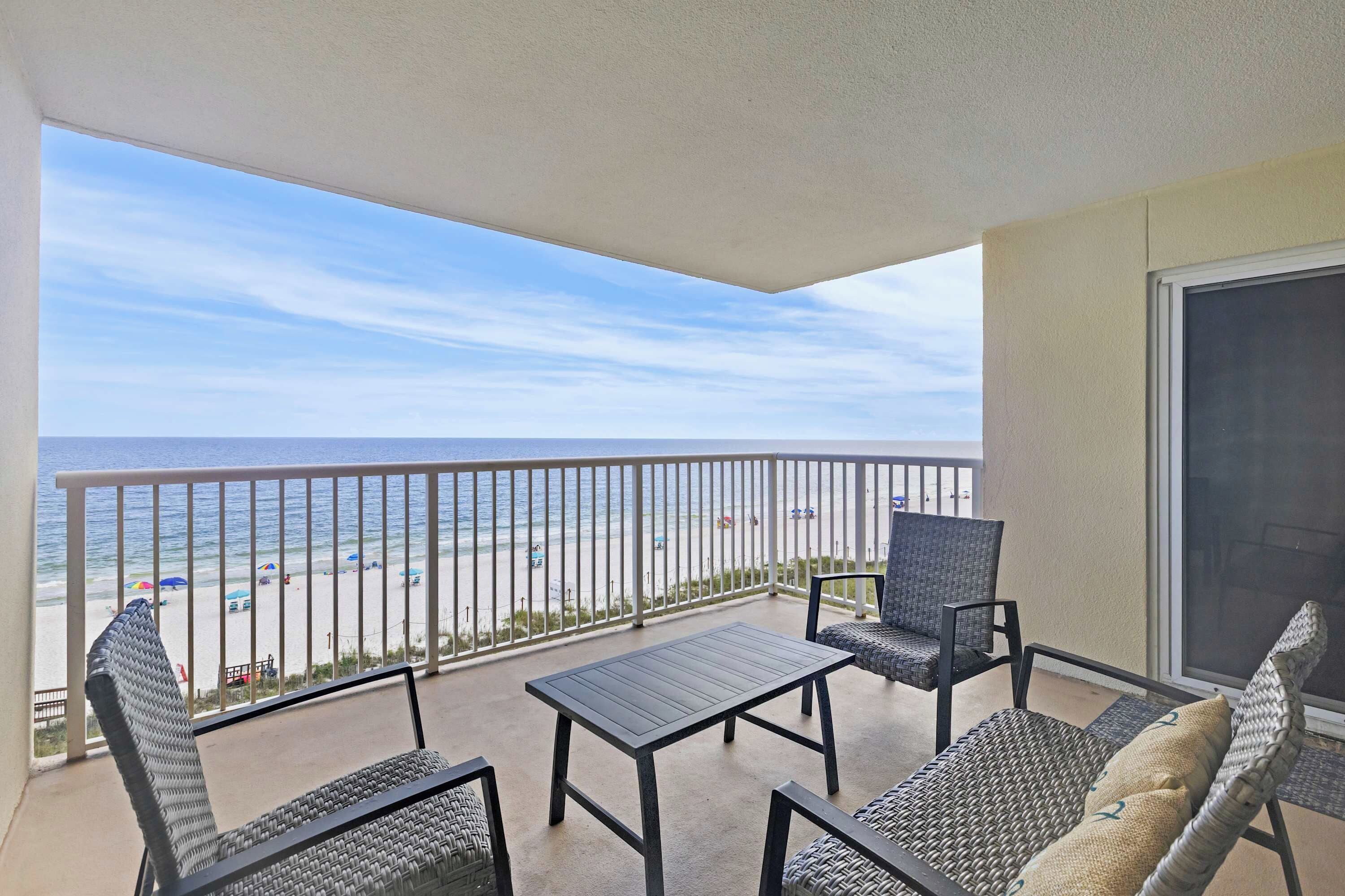 A balcony with a view of the beach, a table, and two chairs.