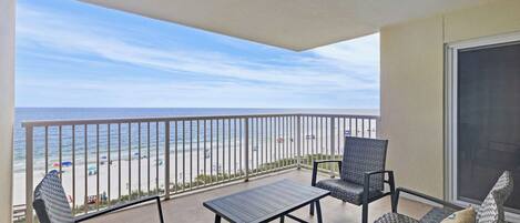 A balcony with a view of the beach, a table, and two chairs.