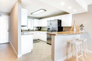 A modern kitchen with white cabinets, a stainless steel refrigerator, and a granite countertop. - Gorgeous Oceanfront condo with washer/dryer, Gulf-front balcony & pool/hot tub (Perdido Key)