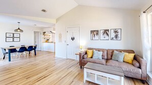 A spacious living area with a wooden floor, a brown leather sofa, a dining table with blue chairs, and a white door. - Updated home near the beach with patio, AC, & private WD (Panama City)