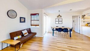 A modern living room with a brown sofa, a wooden coffee table, and a dining area with a wooden table and blue chairs. - Updated home near the beach with patio, AC, & private WD (Panama City)
