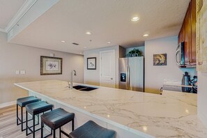 A modern kitchen with a marble countertop, a built-in sink, and bar stools. - Spacious getaway on the Gulf of Mexico with balcony & beach access (Panama City Beach)