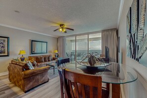 A modern living room with a glass dining table, leather sofa, and a ceiling fan. - Spacious getaway on the Gulf of Mexico with balcony & beach access (Panama City Beach)