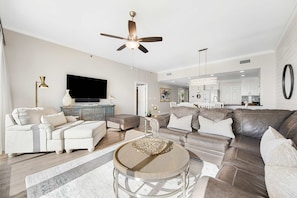 A spacious living room with a large sofa, a coffee table, and a television. - Waterfront condo with pool & hot tub access, Gulf views, W/D, & central AC (Panama City Beach)