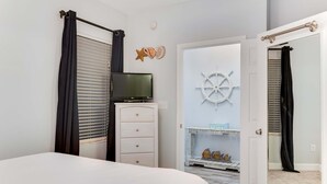 Un dormitorio con cama, cómoda, televisor, puerta con espejo y decoración de pared temática náutica.