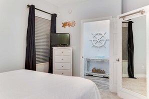 Een slaapkamer met een bed, een dressoir, een televisie, een deur met een spiegel en decoratie aan de muur met een nautisch thema.