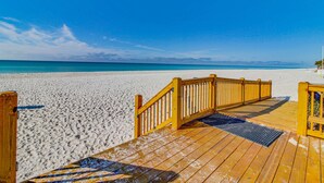 Una passerella di legno che conduce a una spiaggia sabbiosa sotto un cielo azzurro limpido.