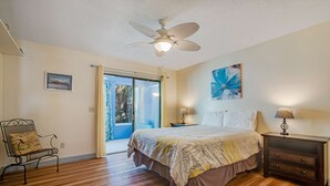 Una camera da letto con un letto, un comodino, una sedia, una ventola a soffitto e vista attraverso una porta scorrevole.
