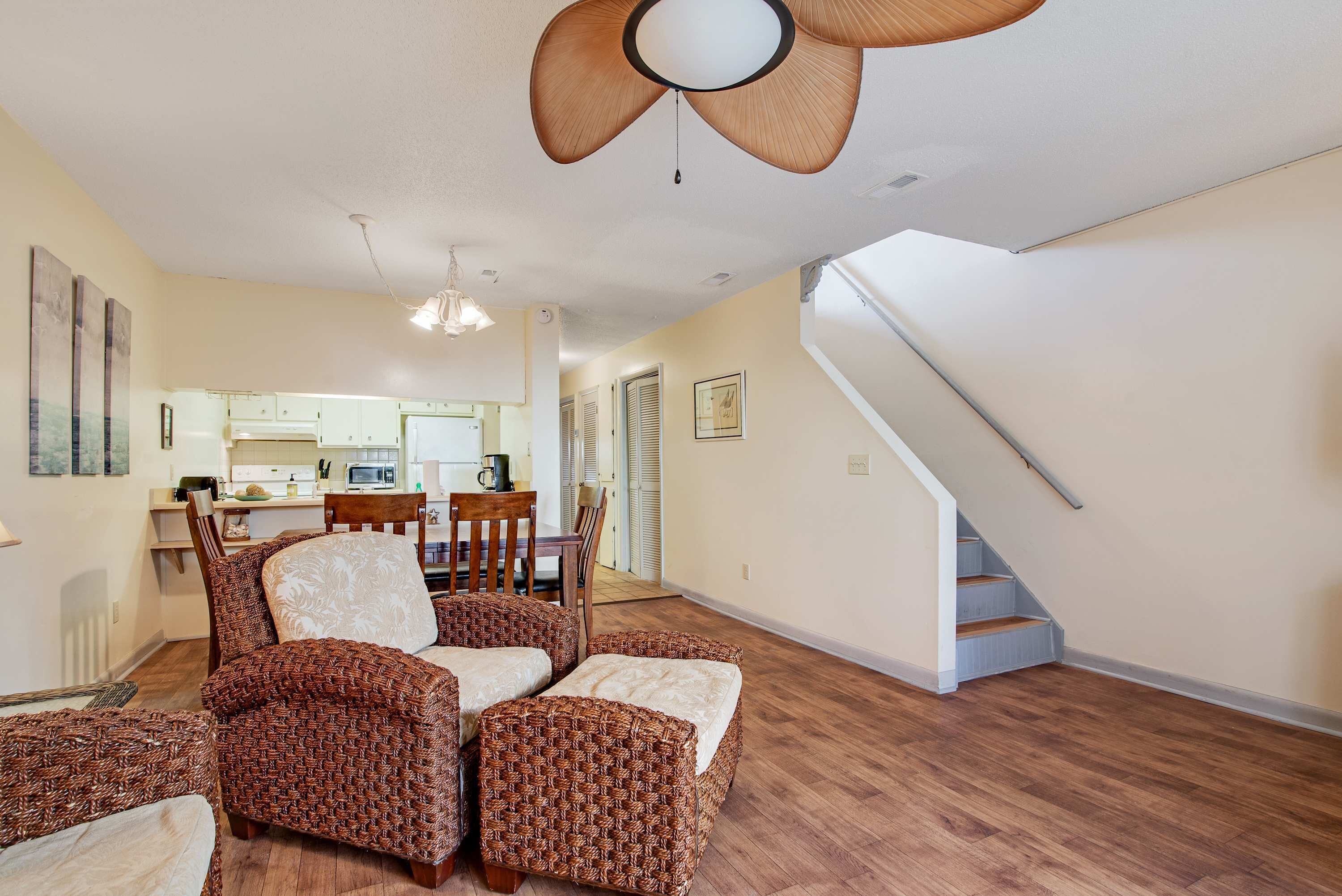 A spacious living room with wicker furniture, a ceiling fan, and a staircase leading to another level.