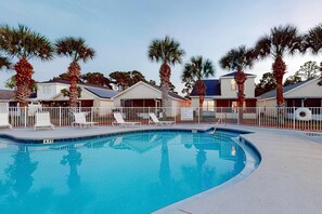 A swimming pool with lounge chairs and palm trees, surrounded by single-story houses with solar panels. - Wonderful vacation retreat close to the beach w/WiFi, central AC, & shared pool (Panama City Beach)