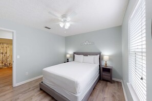 A bedroom with a bed, nightstands, a ceiling fan, and a window with blinds. - Wonderful vacation retreat close to the beach w/WiFi, central AC, & shared pool (Panama City Beach)