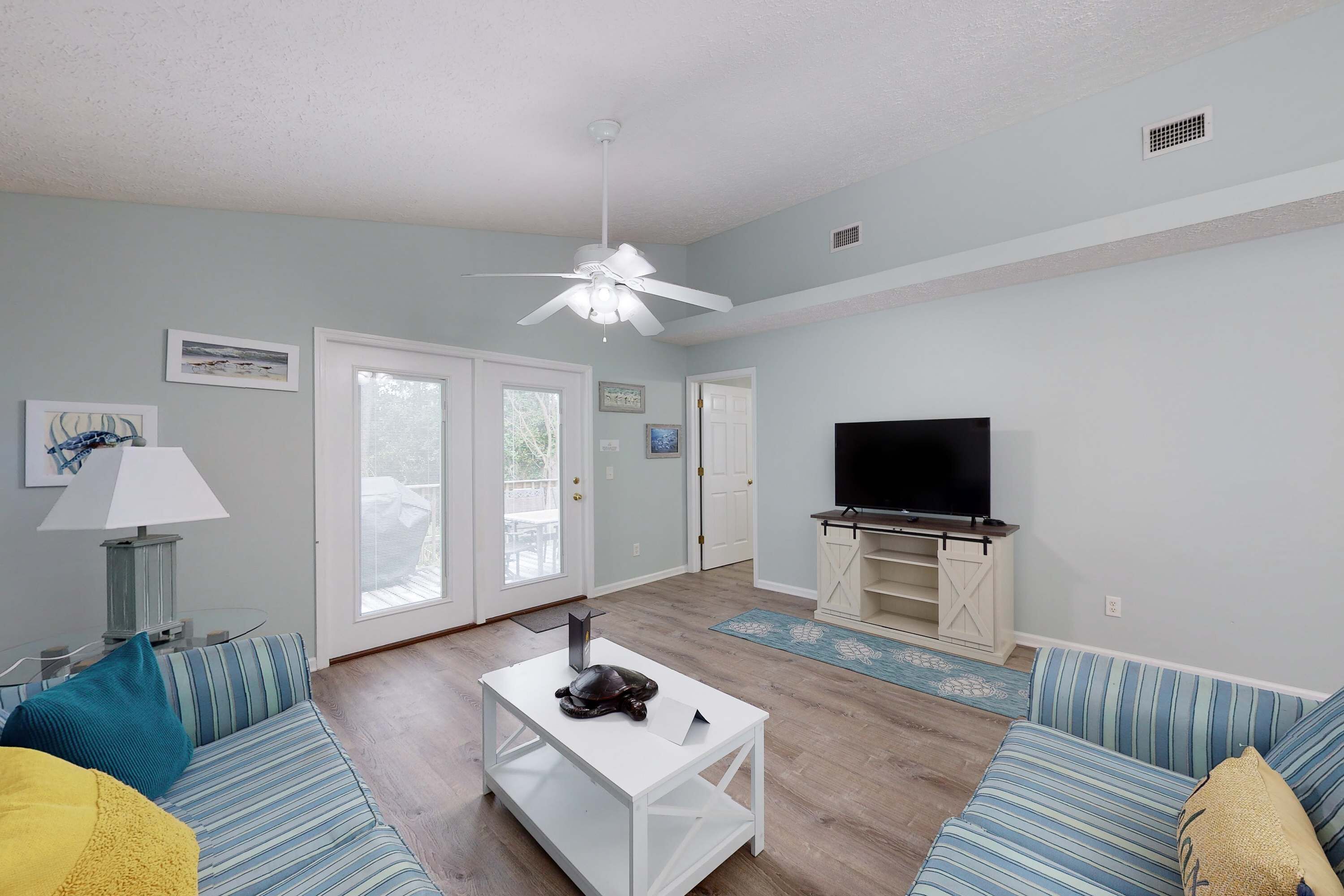 A living room with a ceiling fan, a TV on a wooden stand, a sofa, a coffee table, and a lamp.