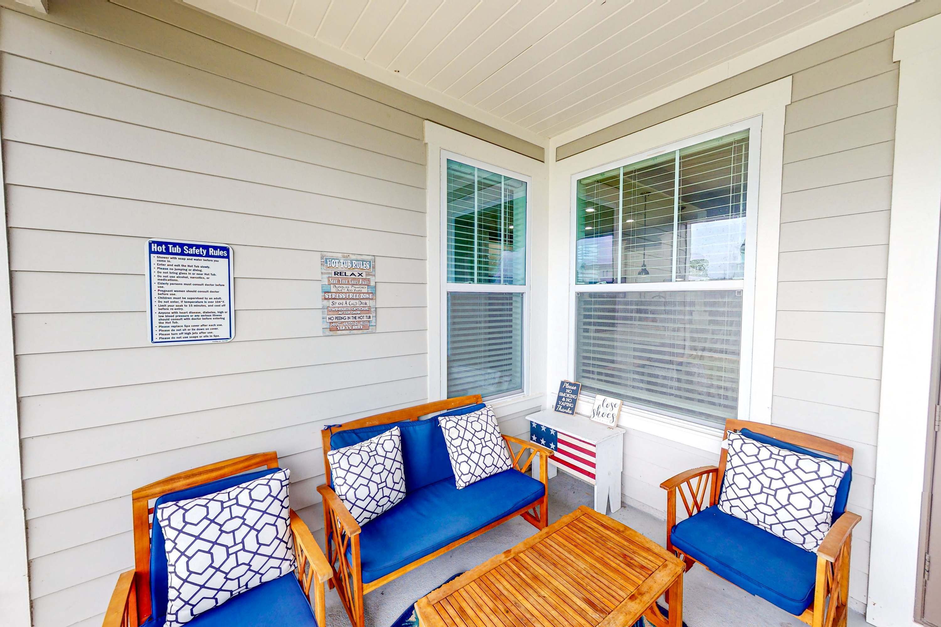 A porch with two wooden chairs and a sofa, each with patterned cushions. There are two signs on the wall, one detailing hot tub safety rules and the other listing rules.