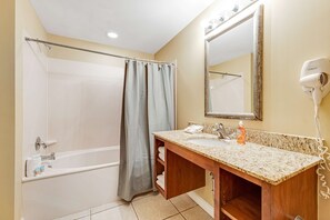 Une salle de bain avec une baignoire, un rideau de douche, un lavabo avec un miroir et un sèche-cheveux fixé au mur.