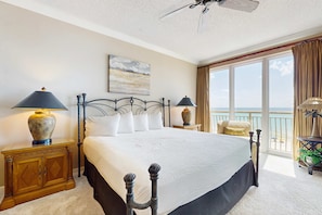 A bedroom with a large bed, two bedside tables with lamps, a ceiling fan, a window with curtains, and a balcony with a view. - Elegant getaway with stunning view, lagoon pool & pickleball - close to shops (Seacrest)