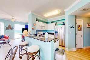 A modern kitchen with a central island, white cabinetry, and a view to the living area. - Ocean-view condo with pools, fitness center and beach access (Panama City Beach)