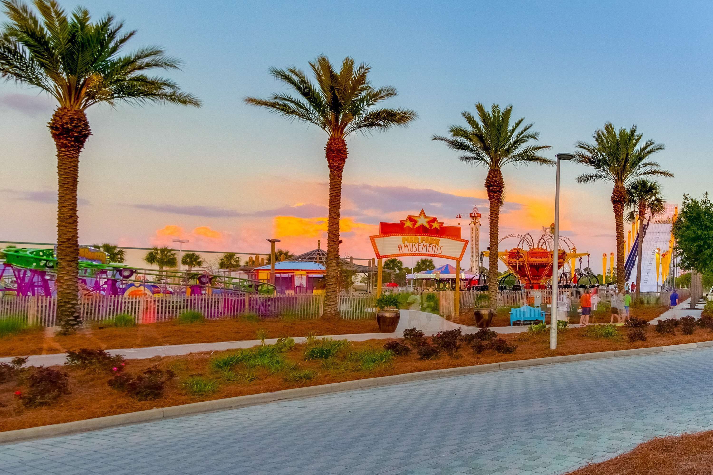 A park with palm trees, a Ferris wheel, and a sign that reads "AMUSEMENTS".