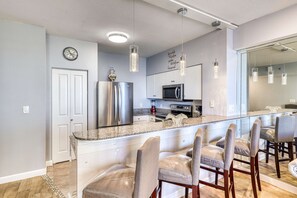 A modern kitchen with stainless steel appliances, a granite countertop, and bar stools. - Lovely beachfront home with balcony, pool, hot tub, & beach (Panama City Beach)