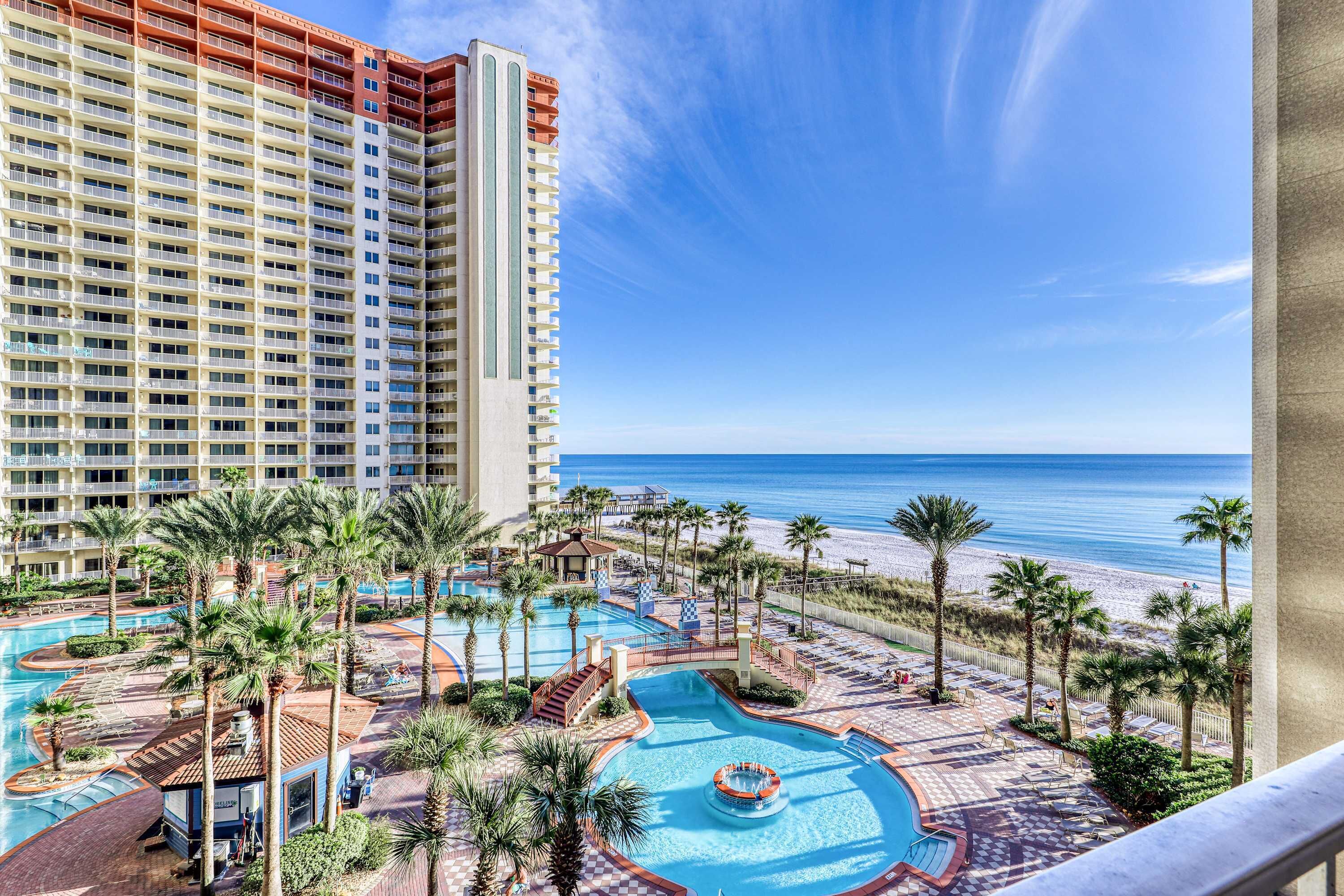 A hotel with a large pool area, palm trees, and a view of the beach.