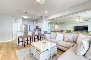 A modern living room with a sofa, a dining table, and chairs. There is a kitchen area with a microwave and a refrigerator. - Lovely beachfront home with balcony, pool, hot tub, & beach (Panama City Beach)