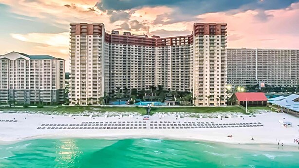 Un hotel di grandi dimensioni con numerosi balconi, una piscina e una spiaggia.