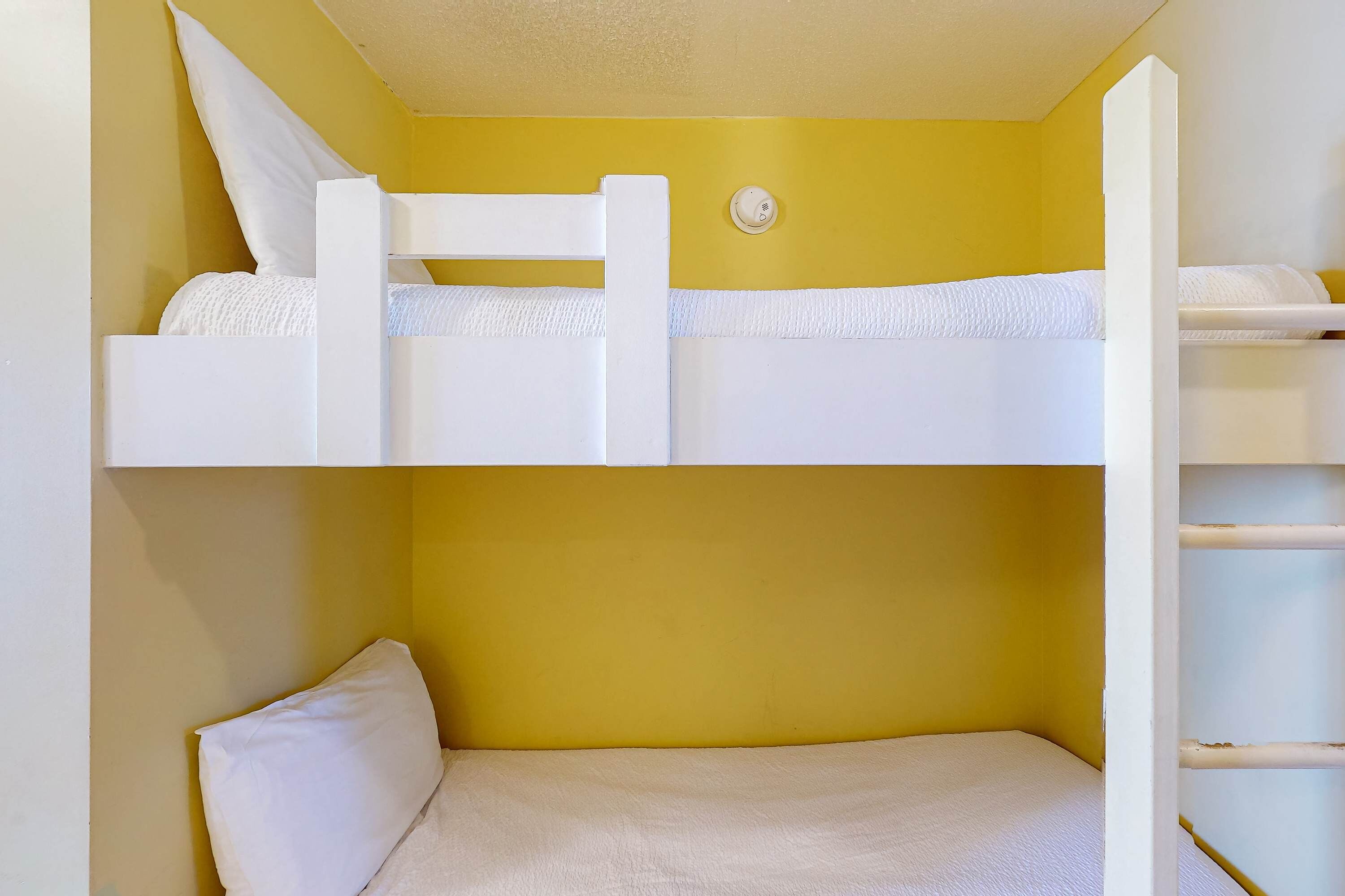 Una cama litera con pared amarilla y ropa de cama blanca.