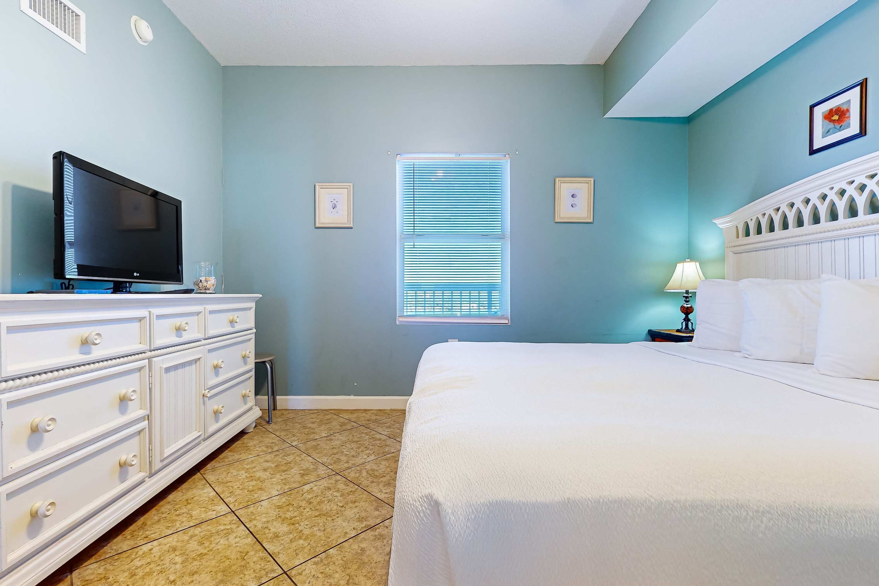 Un dormitorio con cama, cómoda, televisor y ventana con persianas.
