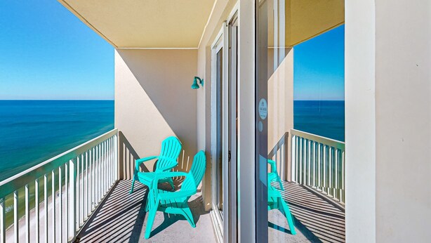 Un balcon avec vue sur l’océan, des chaises turquoise et une porte avec une pancarte.