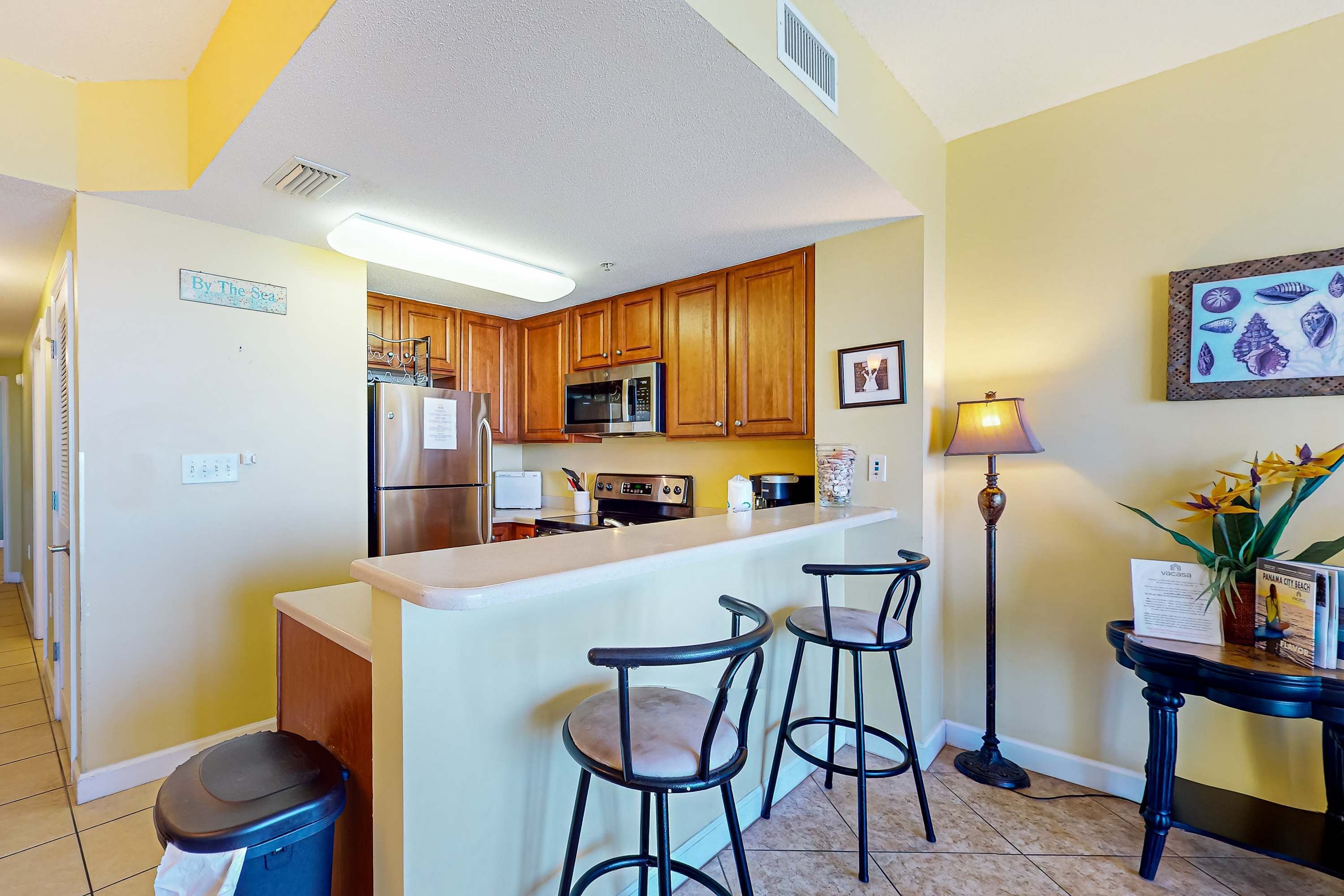A kitchen with wooden cabinets, a microwave, a refrigerator, and a bar area with stools.