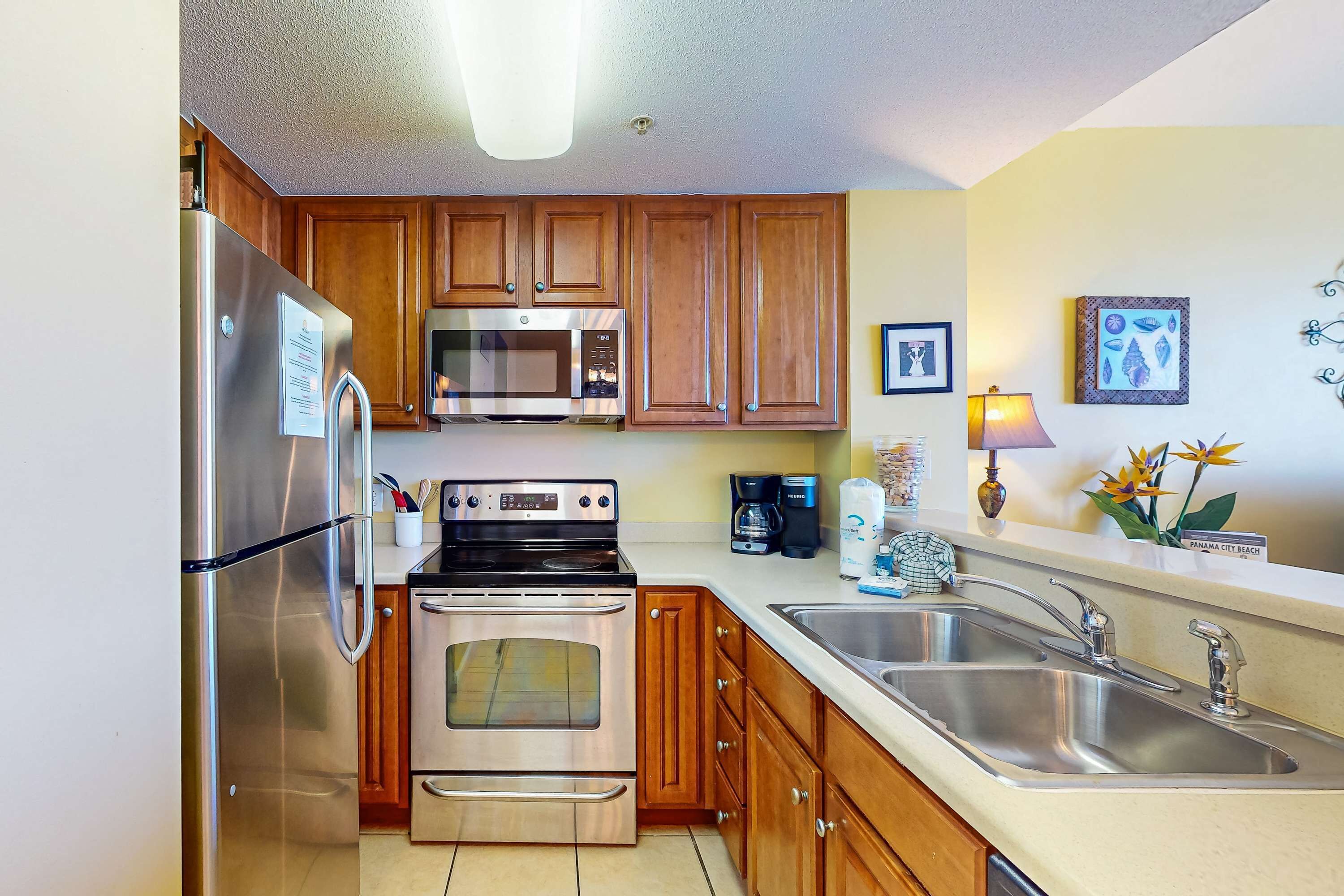A modern kitchen with stainless steel appliances, wooden cabinets, a double sink, and a coffee maker.