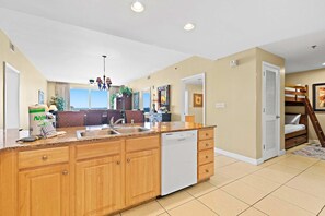 A modern kitchen with wooden cabinets, a dishwasher, and a large window offering a view. - Beachfront resort condo with Gulf views, WiFi, pools, hot tub & lazy river (Panama City Beach)
