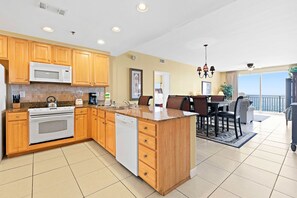 A modern kitchen with wooden cabinets, a built-in microwave, and a dishwasher. - Beachfront resort condo with Gulf views, WiFi, pools, hot tub & lazy river (Panama City Beach)