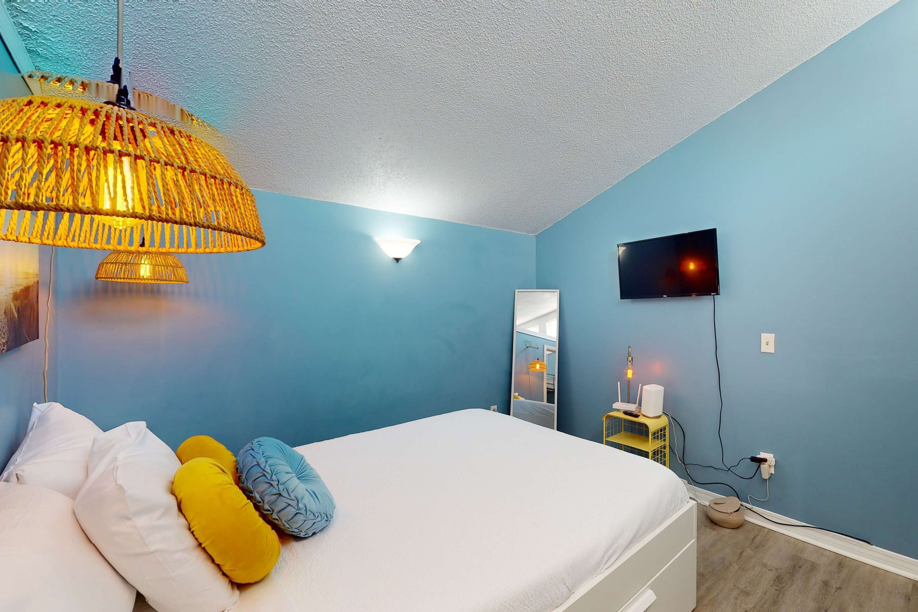 A bedroom with a bed, a hanging lamp, a TV, and a bedside table with a lamp.