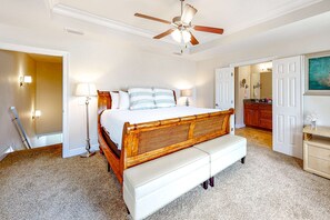 A bedroom with a wooden bed, a white bench, a ceiling fan, and a bathroom visible through an open door. - Dog-friendly beach house with balcony, fenced yard, & AC - walk to beach (Panama City Beach)