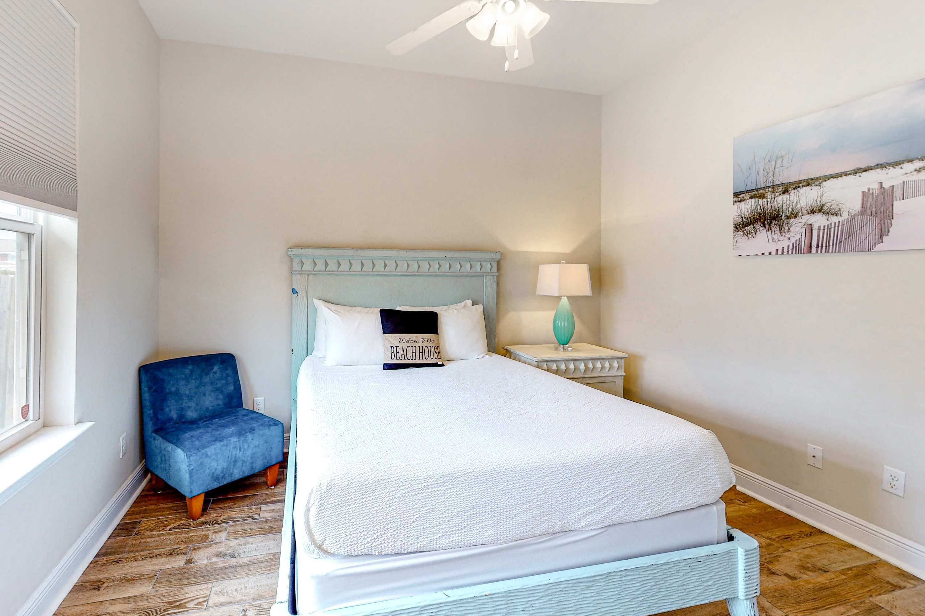 A bedroom with a bed, a blue chair, a nightstand, a lamp, and a painting on the wall.