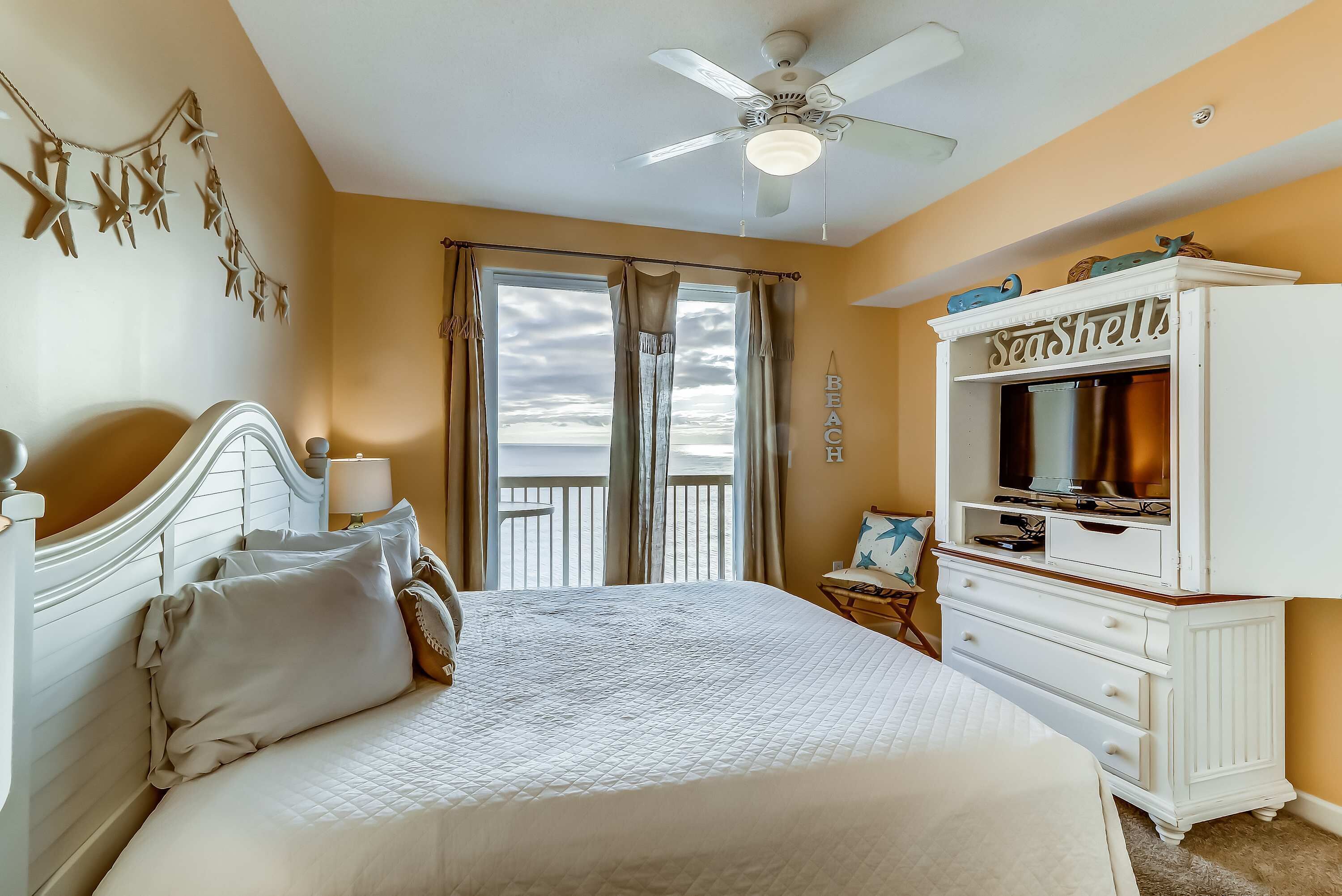 Un dormitorio con cama, cómoda, ventilador de techo y vista a la playa.