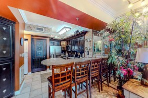A kitchen with dark wooden cabinets, a central island with bar stools, and a large potted plant. - Gulf-front condo with sweeping views, pools, hot tubs, & easy beach (Panama City Beach)