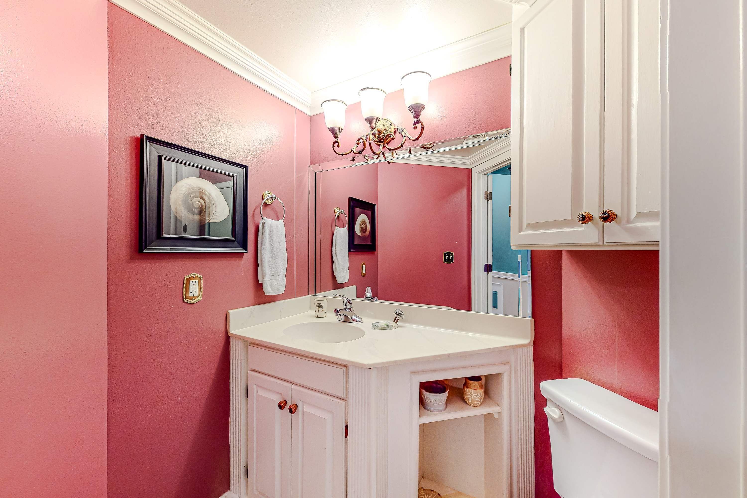 A bathroom with a pink wall, white vanity, and a white toilet.