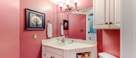 A bathroom with a pink wall, white vanity, and a white toilet.