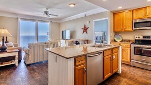 A modern kitchen with wooden cabinets, a large island, and a ceiling fan. - Gulf-front condo with pier views, balcony, heated pool, gym & AC (Panama City Beach)