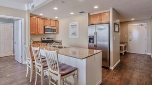 A kitchen with wooden cabinets, stainless steel appliances, and a central island with bar stools. - Gulf-front condo with pier views, balcony, heated pool, gym & AC (Panama City Beach)