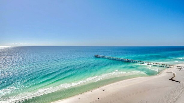 A beach with a long pier extending into the ocean, clear skies, and calm waters. - Gulf-front condo with pier views, balcony, heated pool, gym & AC (Panama City Beach)