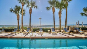 A poolside area with lounge chairs and palm trees, overlooking a beach. - Gulf-front condo with pier views, balcony, heated pool, gym & AC (Panama City Beach)