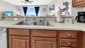 Una cucina con un lavello doppio, mobili in legno, una ventola a soffitto e vista sull'oceano dalle finestre.