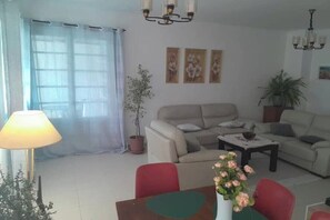 A living room with a sofa, a coffee table, and a dining table with chairs. There are three framed pictures on the wall.
