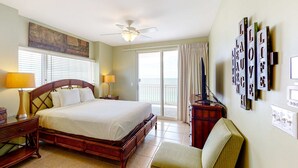 Hotelkamer met een groot bed, twee nachtkastjes, een stoel, een plafondventilator, een raam met zonwering en een muur met ingelijste tekst.