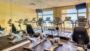 Et fitnesscenter med flere træningsmaskiner, store vinduer og udsigt til havet.