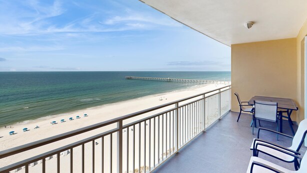 En balkon med udsigt over stranden og havet, et bord med stole og et gelænder.