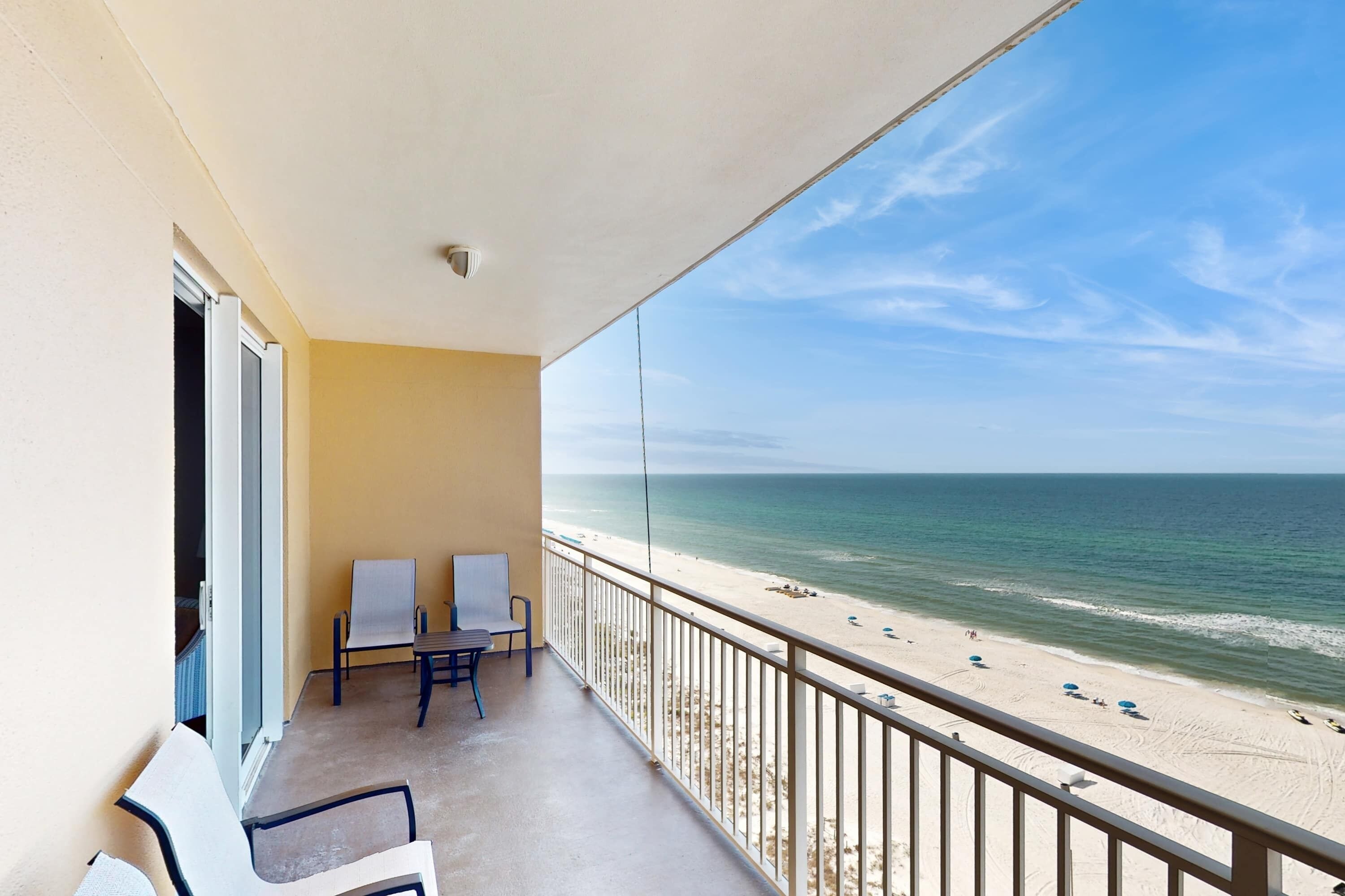 A balcony with a view of the beach, a table, two chairs, and a whiteboard.