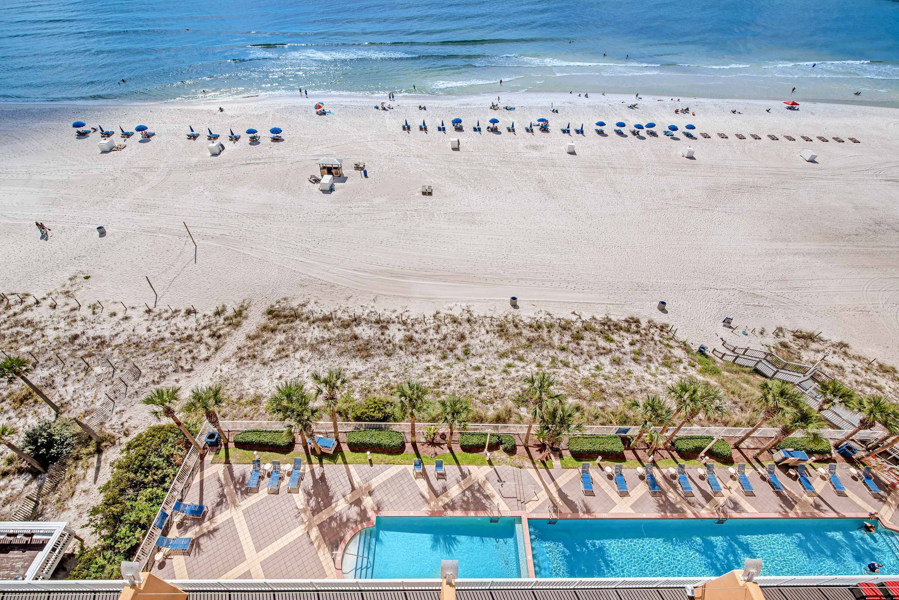 A beach resort with a swimming pool, sun loungers, and a sandy beach.